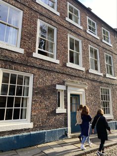 two people walking down the sidewalk in front of a brick building with windows on each side