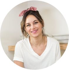 a woman with a pink bow in her hair smiles at the camera while wearing a white v - neck shirt