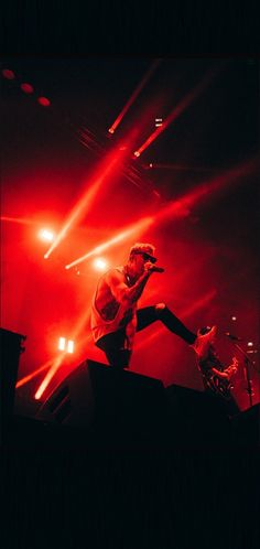 a man standing on top of a stage with his legs in the air and lights behind him