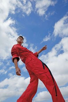 a man in red jumpsuit playing frisbee against a blue sky with clouds