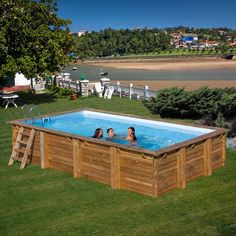 three people in a wooden swimming pool surrounded by green grass and trees, overlooking the water