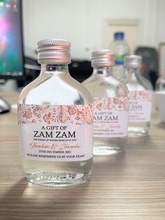 three bottles of water sitting on top of a wooden table next to a computer monitor