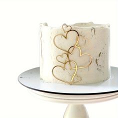 a white cake with gold hearts on it sitting on top of a table next to a plate