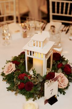 a white lantern with flowers and greenery is on the table at a wedding reception