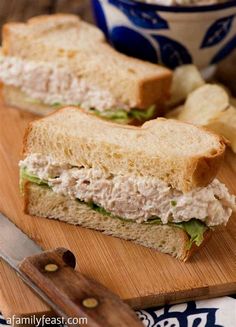 a sandwich cut in half sitting on top of a wooden cutting board next to chips