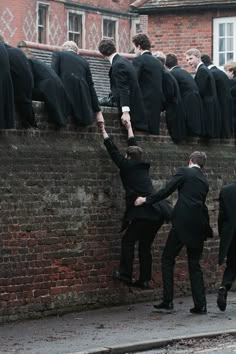 a group of men in suits climbing up the side of a brick wall with their arms raised