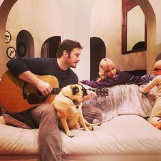 a man sitting on a bed while playing guitar with two children and a dog in front of him