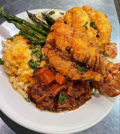 a white plate topped with fried chicken, potatoes and asparagus next to mashed potatoes