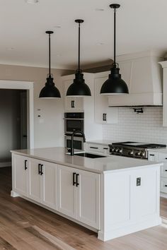 a large kitchen with white cabinets and black pendant lights over the stove top island in front of an oven