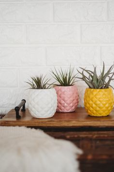 three pineapple shaped planters sitting on top of a wooden table next to a white brick wall