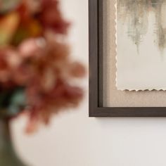 a vase filled with flowers sitting next to a framed piece of paper on a wall