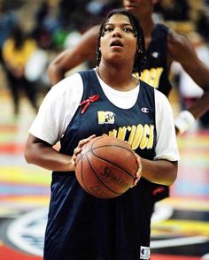 a woman holding a basketball while standing on top of a basketball court in front of other people