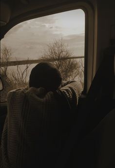 a person sitting on a bus looking out the window at something in the distance and trees outside