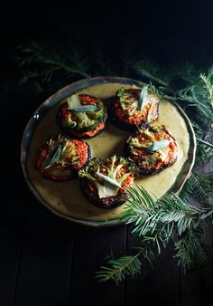 grilled tomatoes and fennel on a plate next to pine branches, dark background