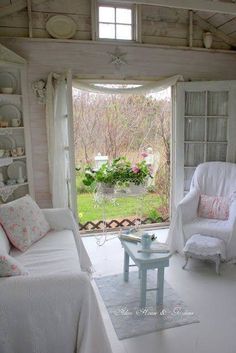 a living room filled with white furniture next to an open door leading to a lush green yard