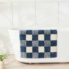 a bathtub with a blue and white checkered rug on the side, next to a potted plant