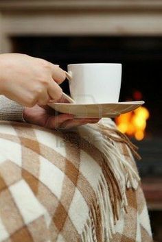 a person holding a cup and saucer on top of a blanket with a fireplace in the background