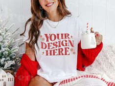 a woman sitting on a bed holding a coffee mug and wearing a t - shirt that says your design here