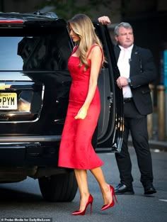 a woman in a red dress stepping out of a black suv with her hand on the door