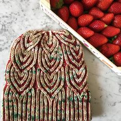 a knitted hat next to a box of strawberries on a marble counter top