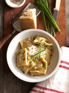 a white bowl filled with ravioli on top of a wooden table next to bread