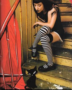 a woman sitting on the steps next to a black cat and wearing tights with striped stockings