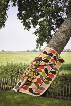 a woman laying on top of a colorful blanket next to a tree in a field