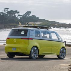 a yellow van with surfboards on top driving down the road next to the ocean