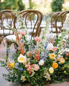 an arrangement of flowers and greenery on the ground in front of chairs at a wedding