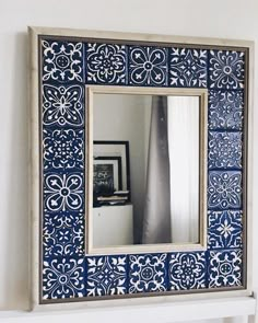 a blue and white tile mirror hanging on the wall next to a shelf with a vase