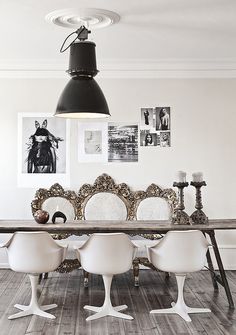 a dining room table with white chairs and pictures on the wall above it, along with an antique chandelier