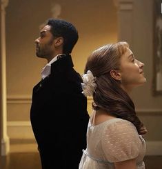 a man in a tuxedo standing next to a woman wearing a dress and flower in her hair