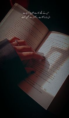 an open book with arabic writing on the pages and a person's hand holding it