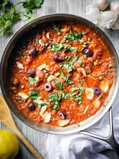 a pan filled with meat and olives on top of a table next to garlic