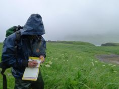 a man in a raincoat is writing on a piece of paper while wearing a backpack