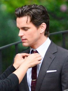 a man adjusts his tie while standing next to a woman