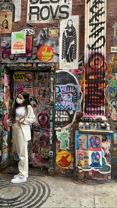 a woman wearing a face mask standing in front of a graffiti covered building