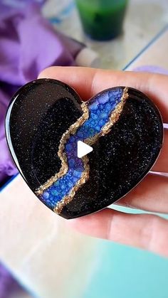 a hand holding a heart shaped brooch with a blue and black design on it