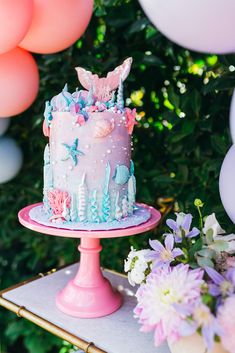 a pink cake sitting on top of a table next to some balloons and other decorations