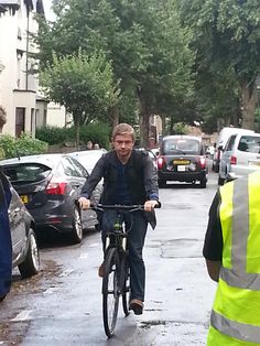 a man riding a bike down a street next to parked cars on a rainy day