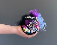 a person's hand holding a small hat with buttons and feathers