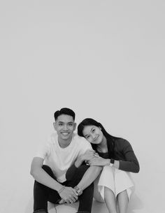 a man and woman sitting next to each other on a white floor with their arms around each other