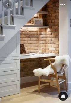 a white chair sitting under a stair case next to a desk and bookshelf