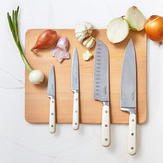 five knives are on a cutting board with garlic and onions