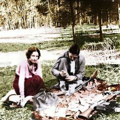 a man and woman sitting on the ground next to a fire