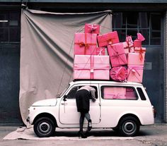 a man standing next to a white car filled with pink wrapped presents on top of it