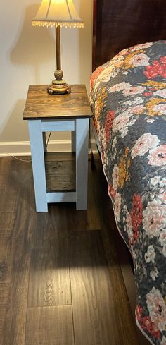 a bed with a floral bedspread next to a night stand on a wooden floor