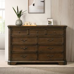 a wooden dresser sitting in a living room next to a painting and potted plant