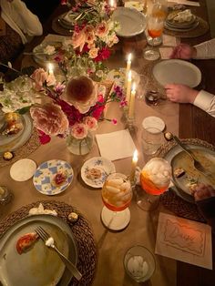 people sitting at a long table with plates and food on it, surrounded by candles