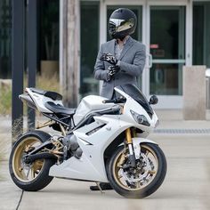 a man in a suit and helmet standing next to a white motorcycle on the street